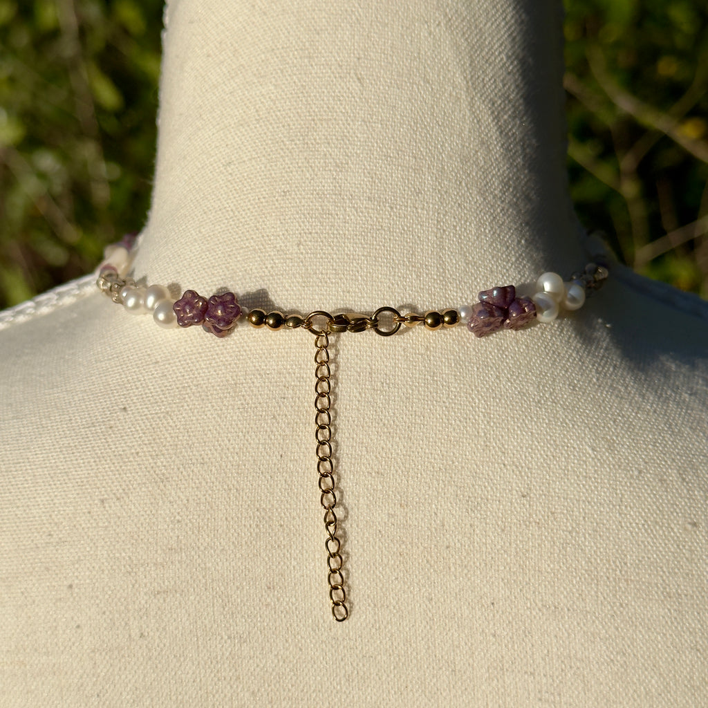 Back of necklace with purple and white beads on a mannequin neck against a natural background