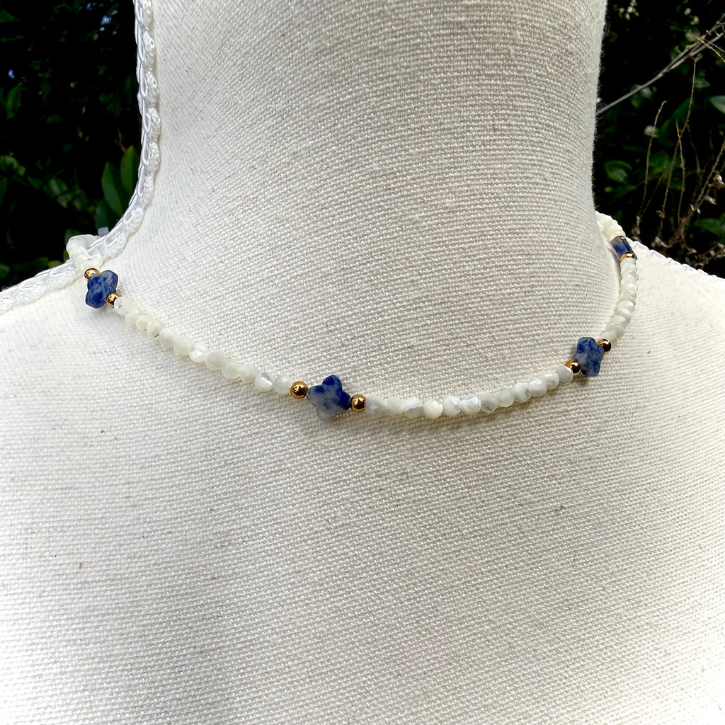 Necklace with white beads and blue and gold accents on a mannequin.