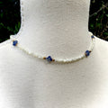 Necklace with white beads and blue and gold accents on a mannequin.