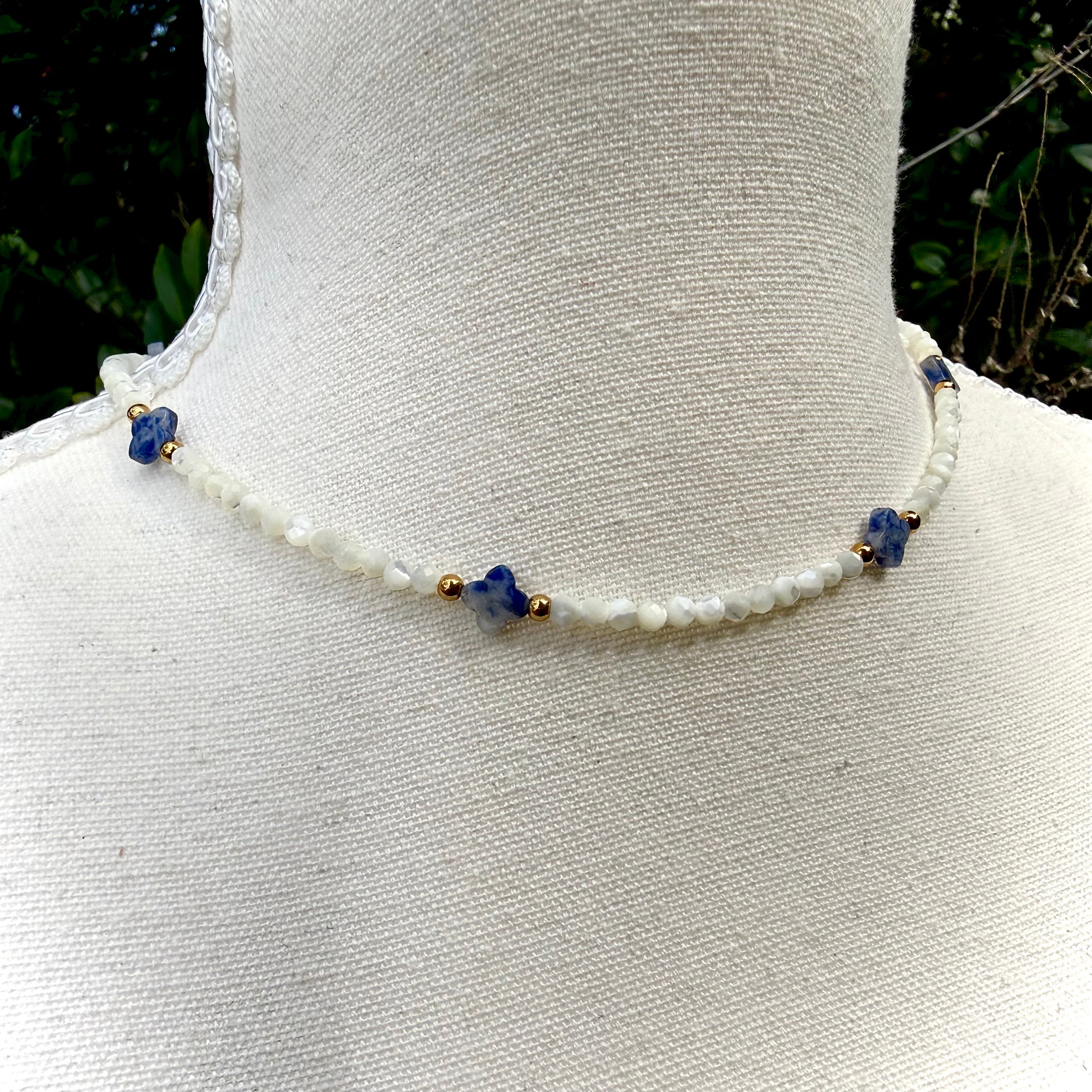 Necklace with white beads and blue and gold accents on a mannequin.
