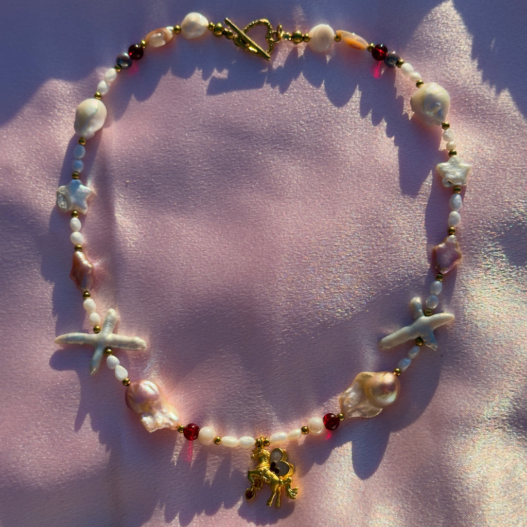 Necklace with starfish and gold horse charm on a pink fabric background