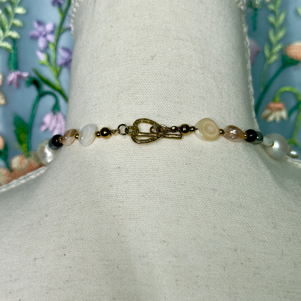 Necklace with pearls and gold clasp on a mannequin bust against a floral background