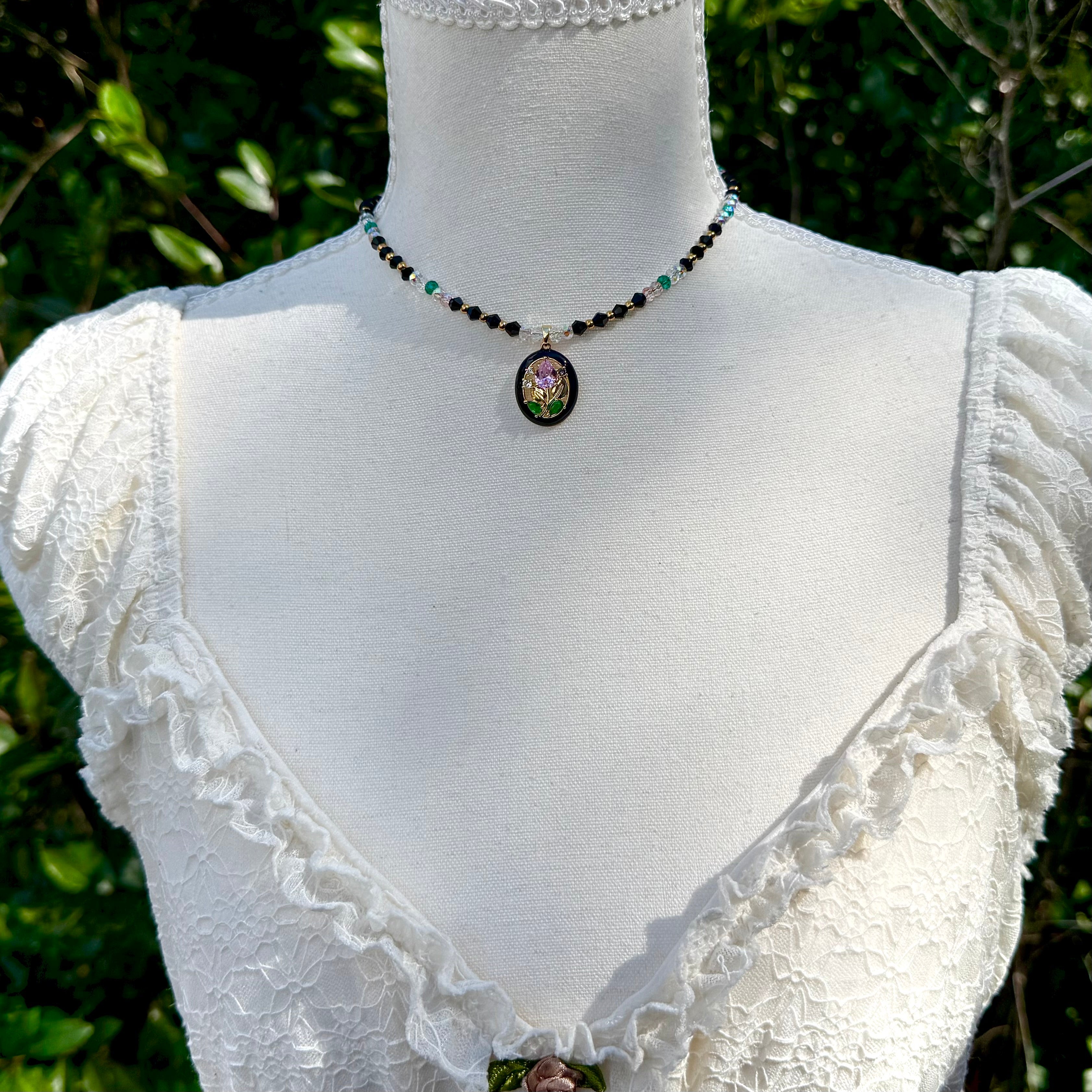 Mannequin wearing a white lace top with a necklace featuring a pendant on a green leafy background