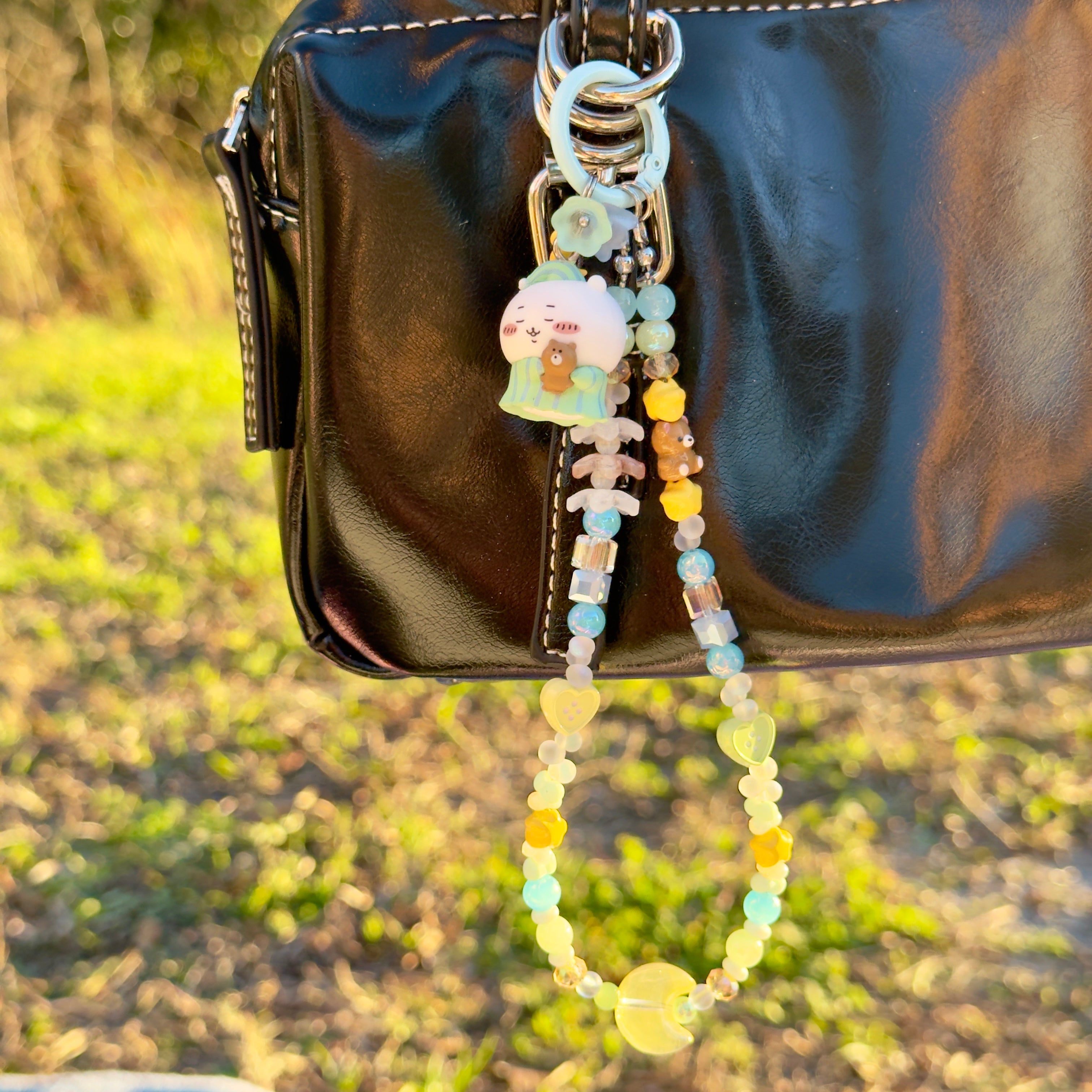 Beaded keychain with a small plush toy attached to a black bag outdoors.