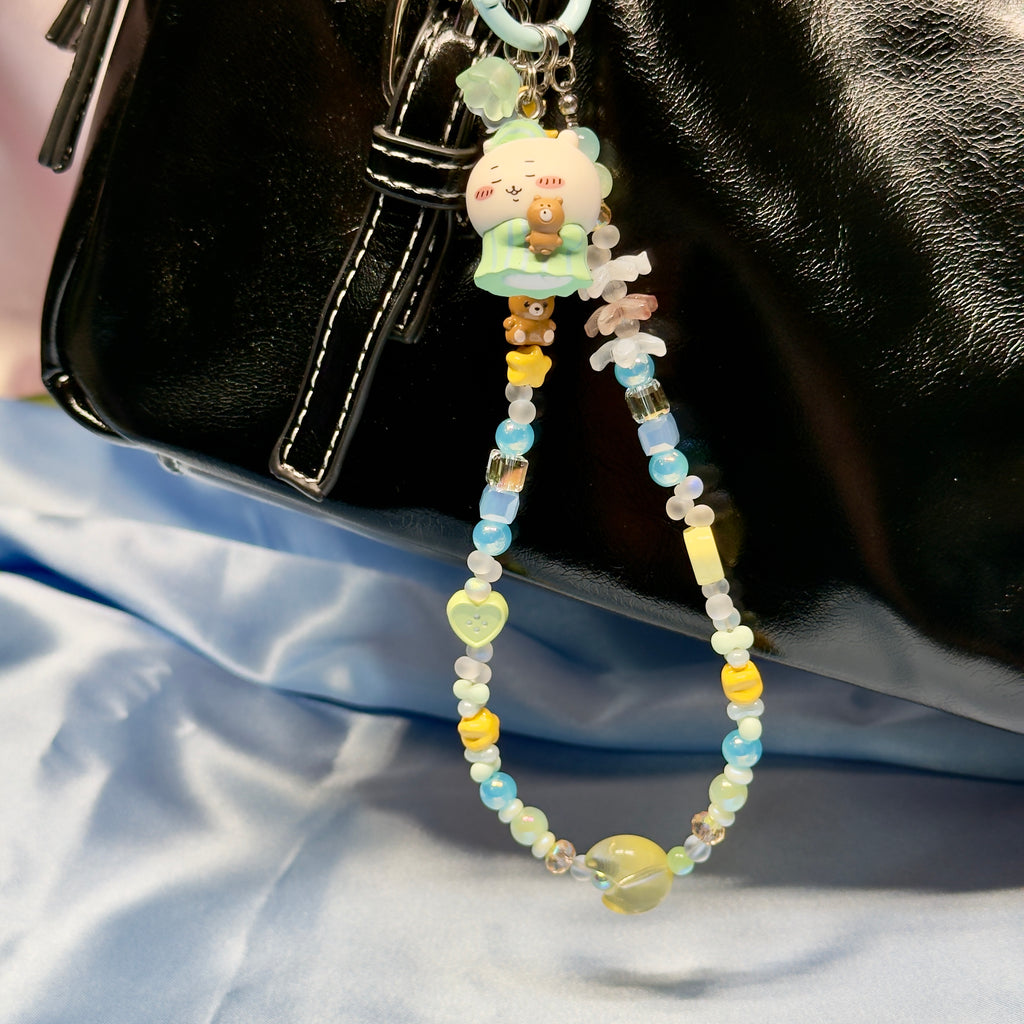 Beaded keychain with cartoon character attached to a black bag on a light blue fabric background