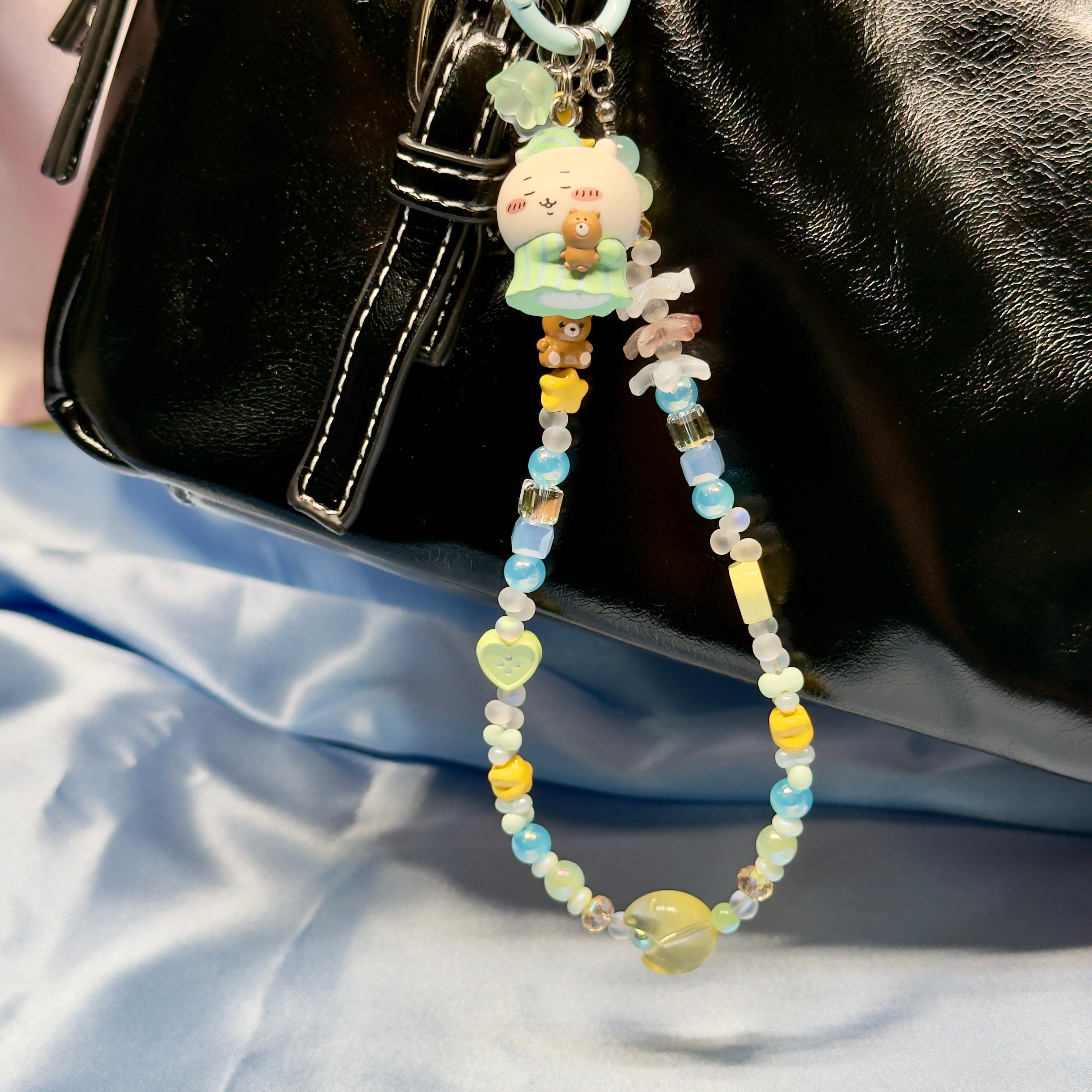 Beaded keychain with cartoon character attached to a black bag on a light blue fabric background