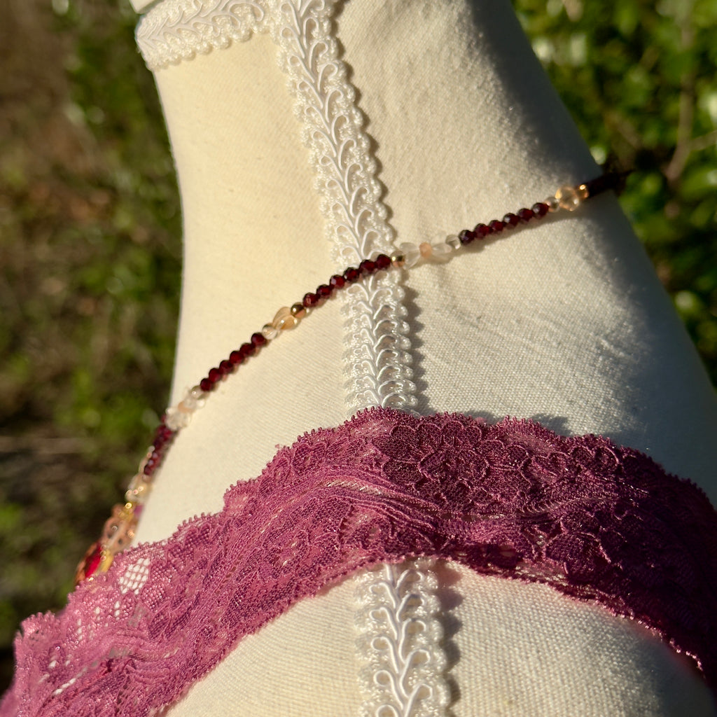 Mannequin wearing a lace garment with a beaded necklace against a blurred natural background