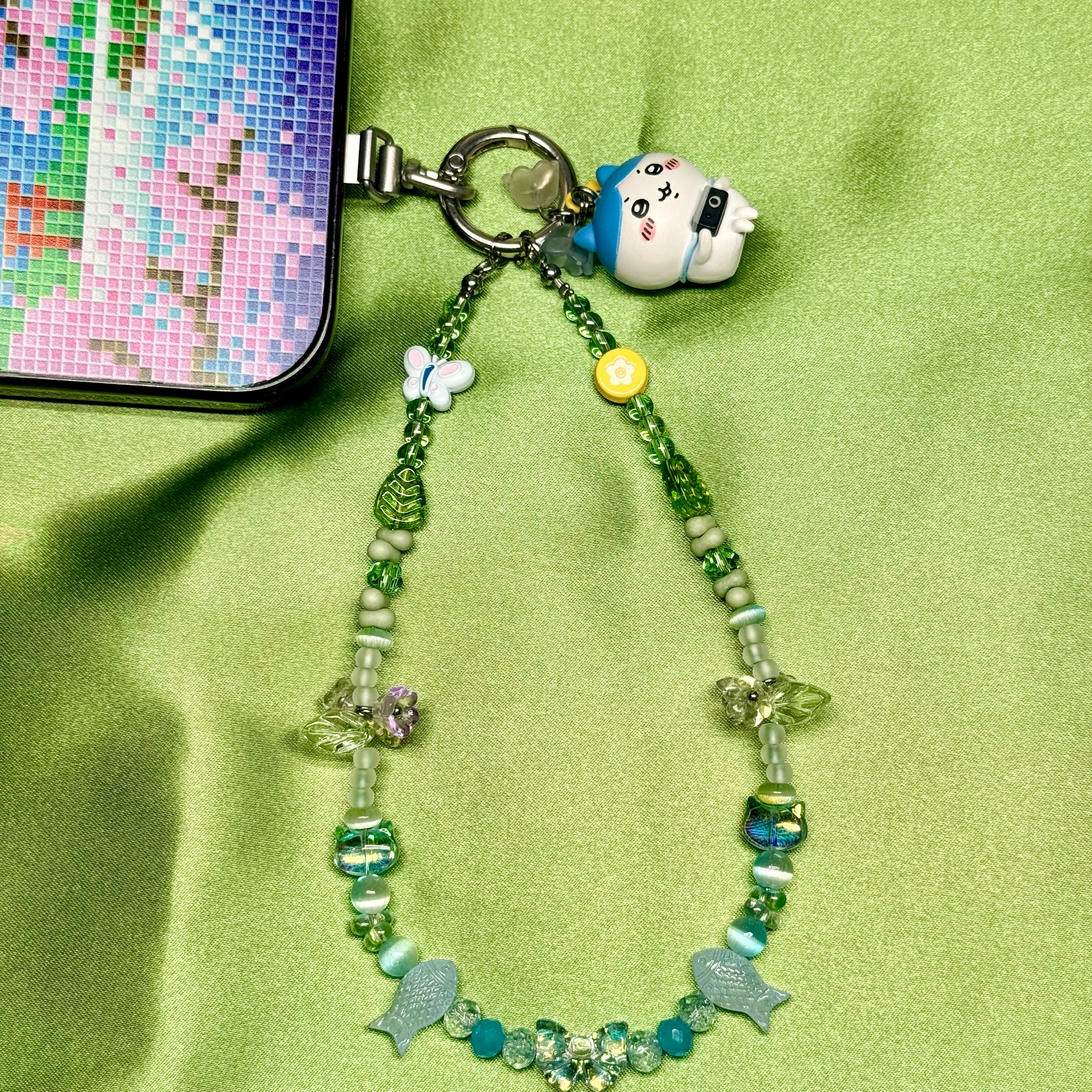 Phone charm with beads and a small figurine on a green background