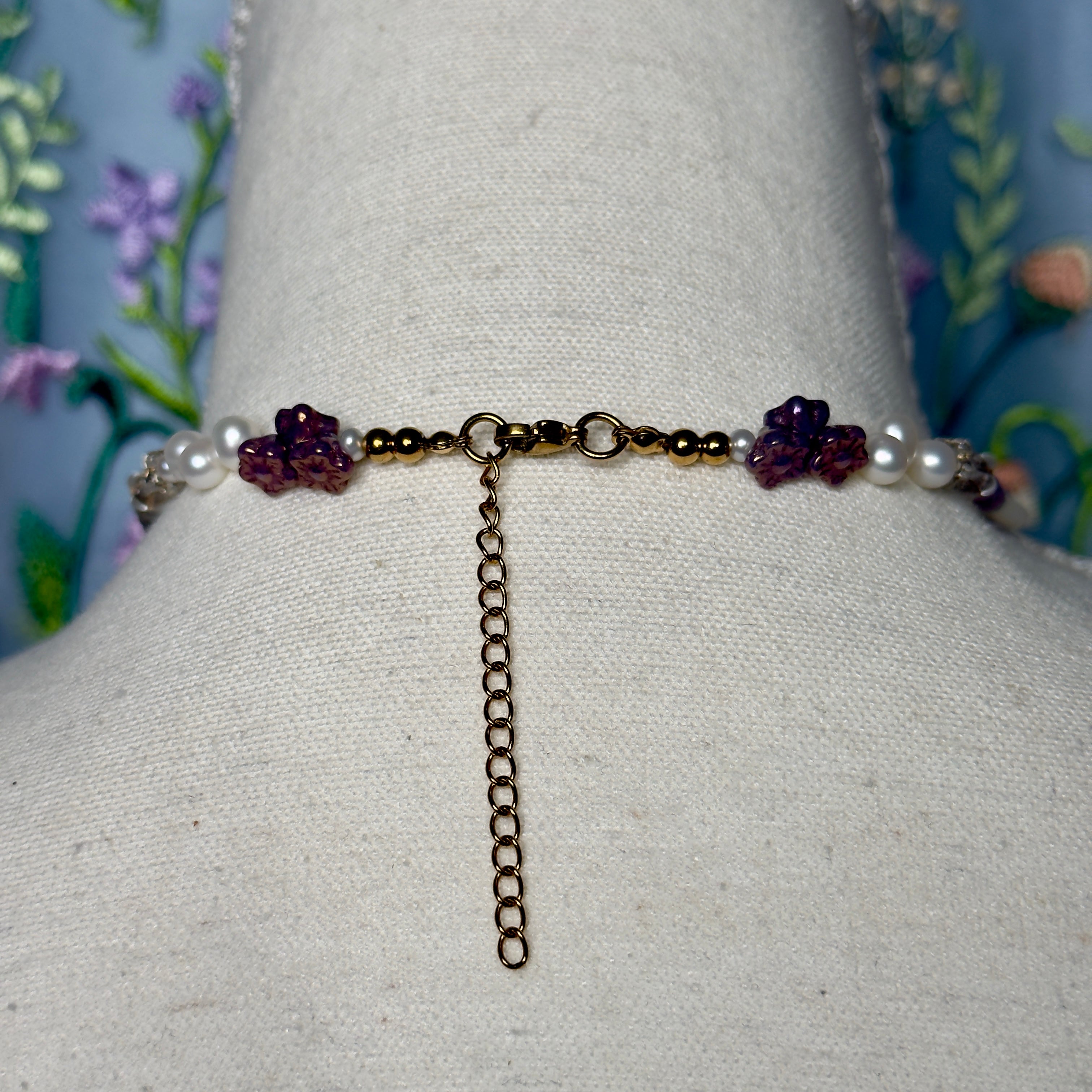 Back of a necklace with pearls and purple beads on a mannequin against a floral background