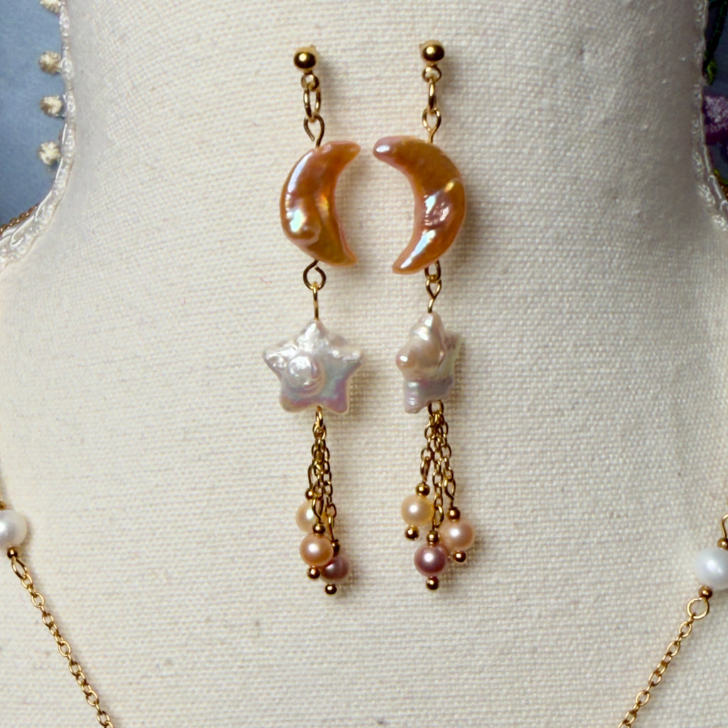 Pair of earrings with crescent moon design and pearl-like beads on a mannequin bust.