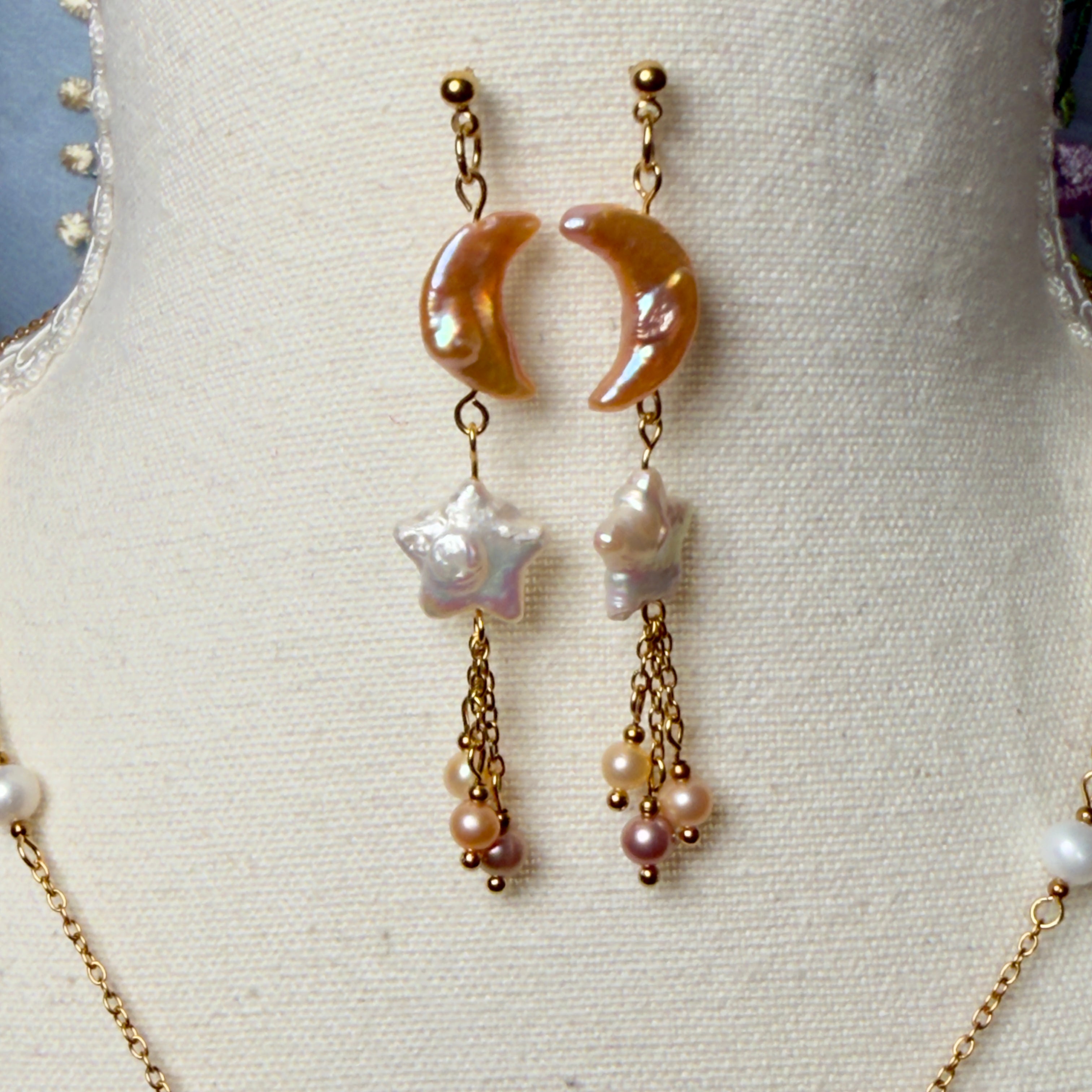 Pair of earrings with crescent moon design and pearl-like beads on a mannequin bust.