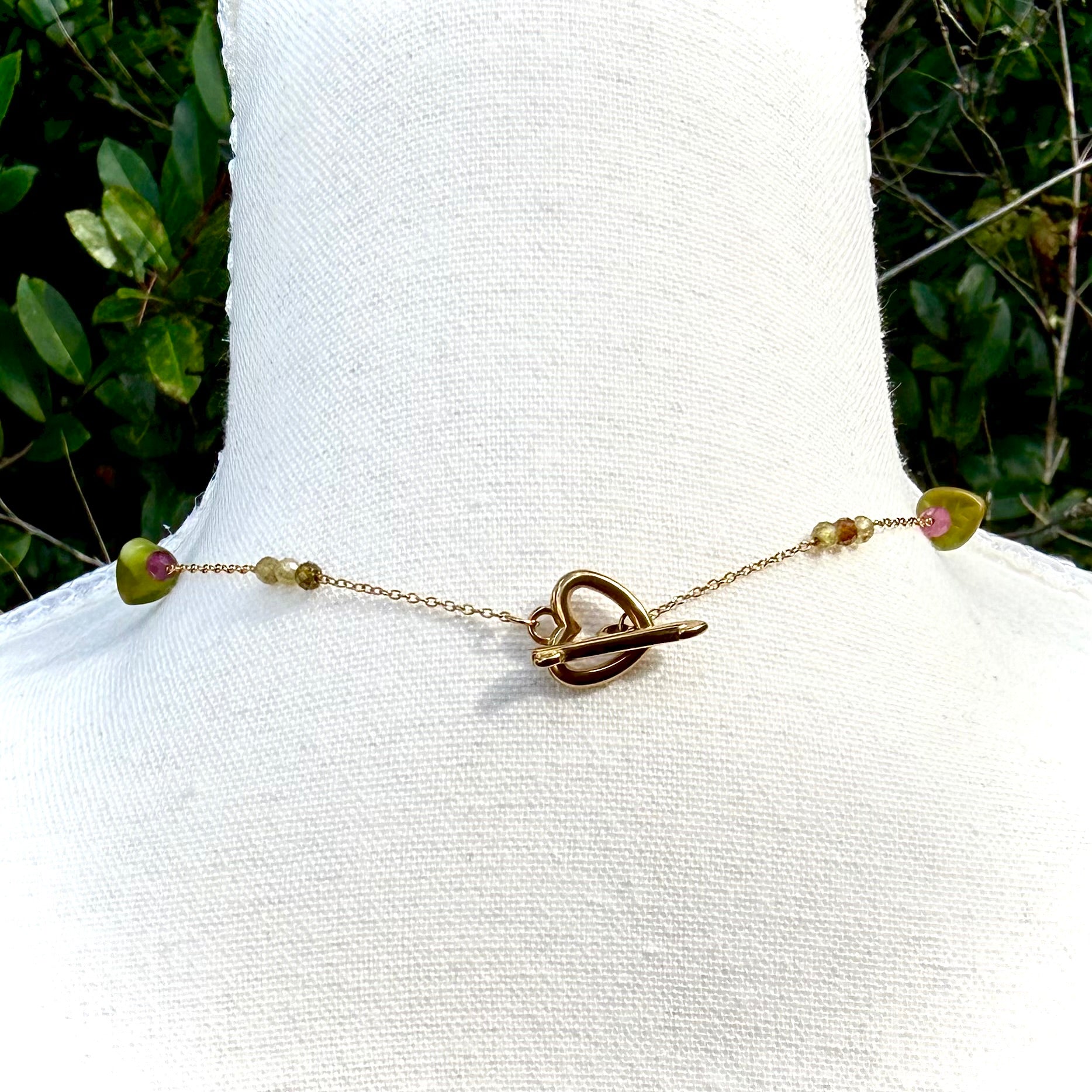 Gold necklace with heart clasp on a mannequin against a green leafy background