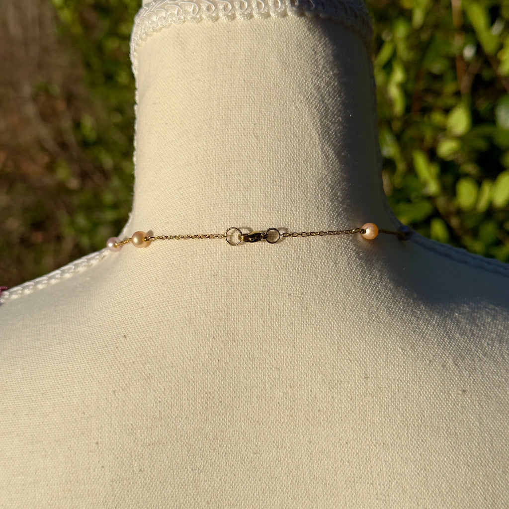 Gold chain necklace with pearls on a mannequin bust against a blurred green outdoor background