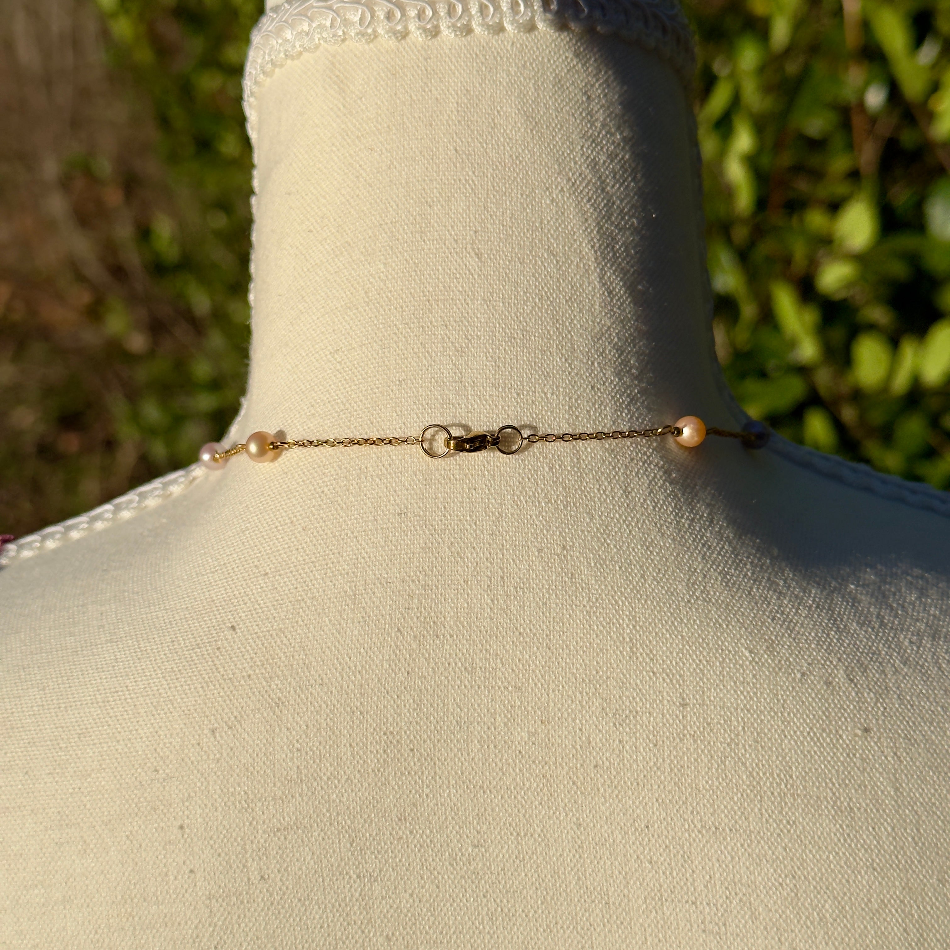 Gold chain necklace with pearls on a mannequin bust against a blurred green outdoor background