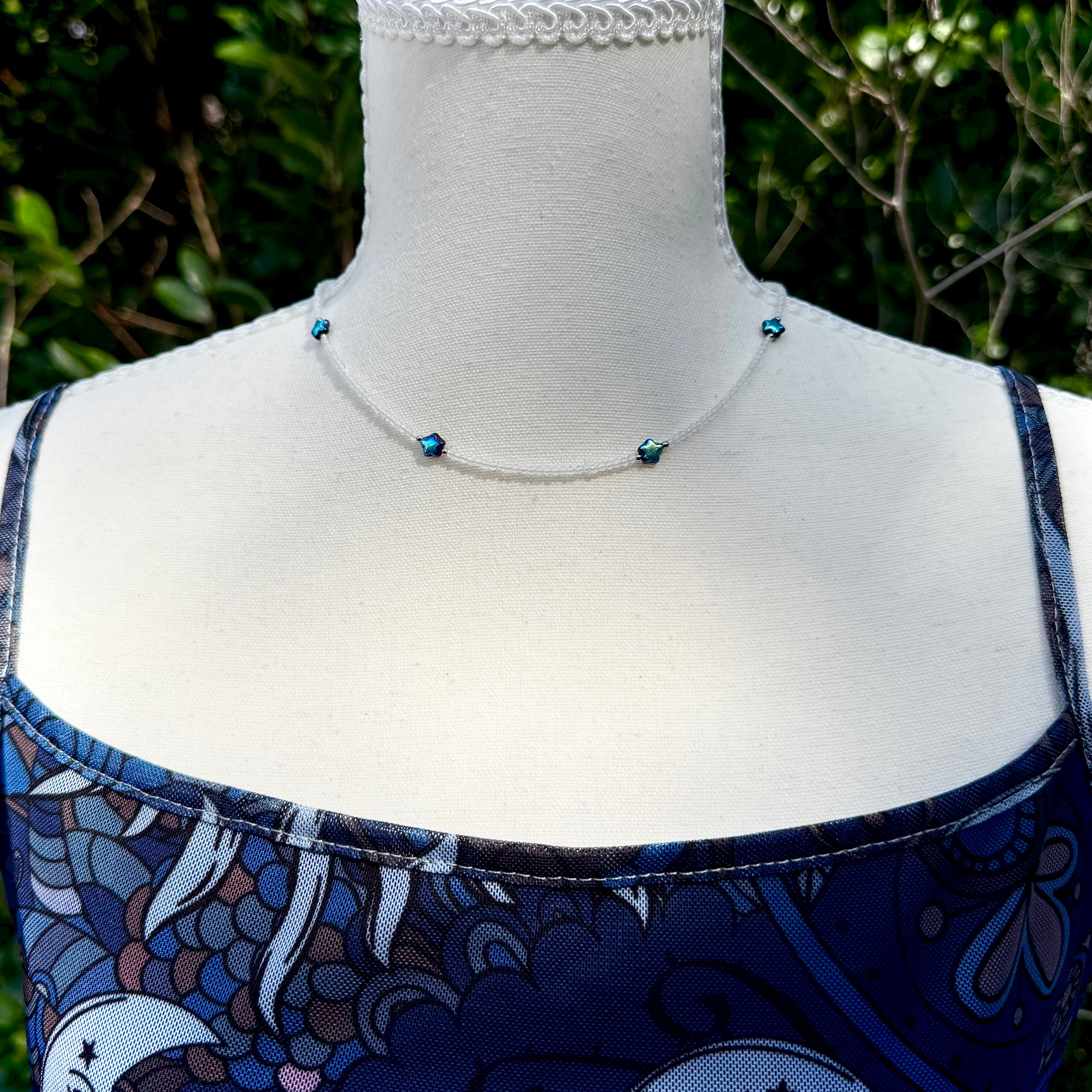 Necklace on a mannequin with a blue patterned dress against a green leafy background