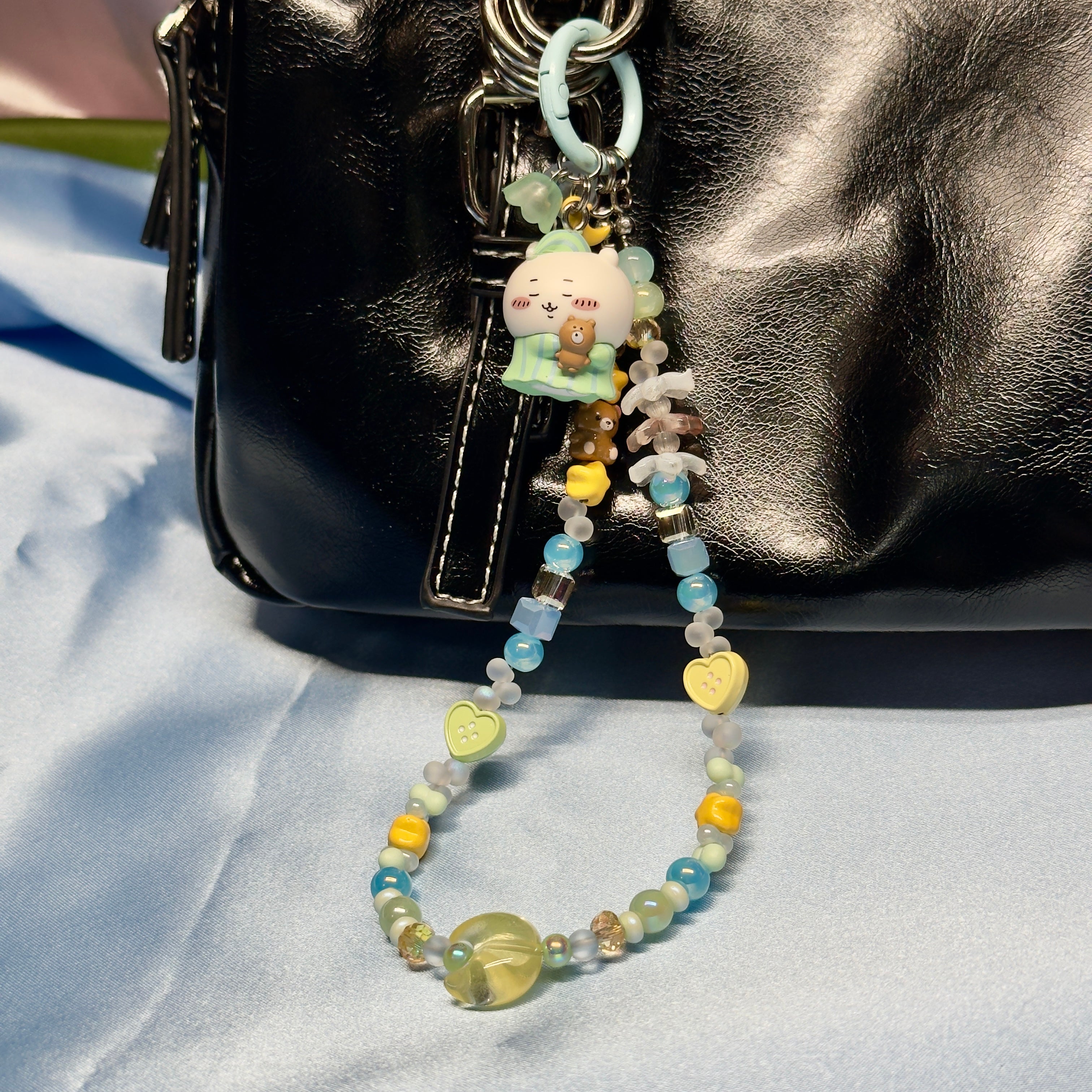 Beaded keychain with cartoon character attached to a black bag on a light blue fabric background