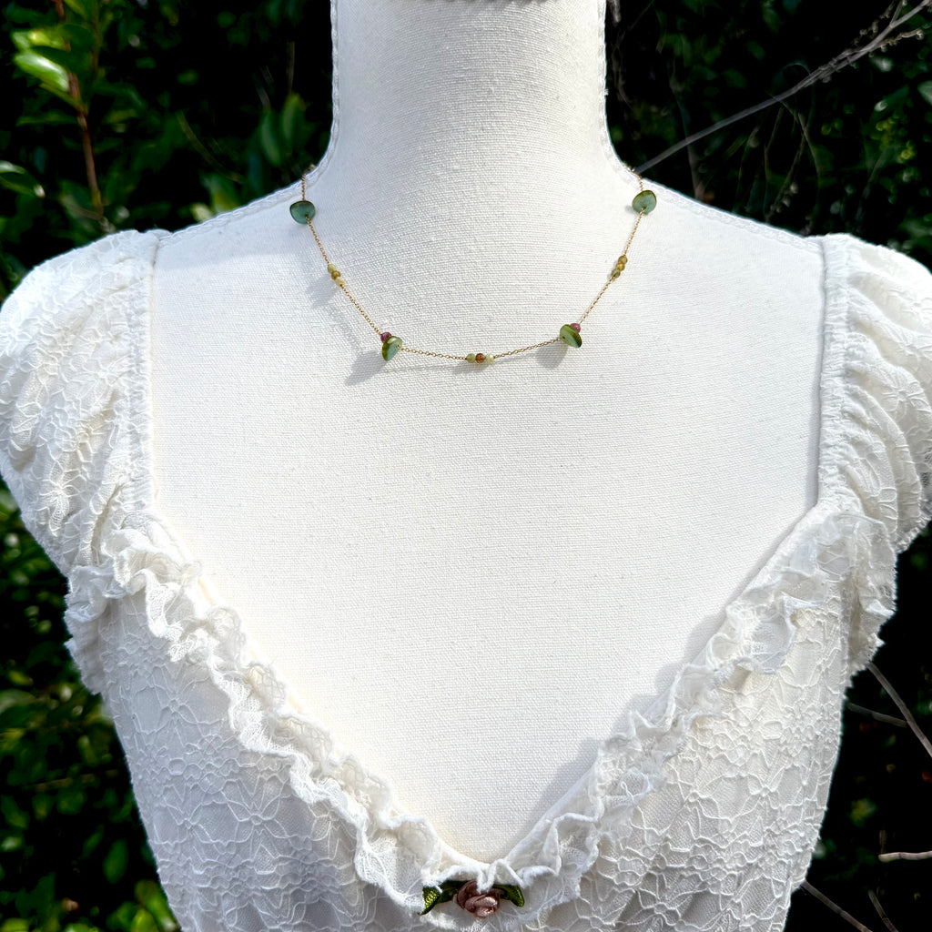 Mannequin wearing a white lace top with a green necklace against a blurred natural background