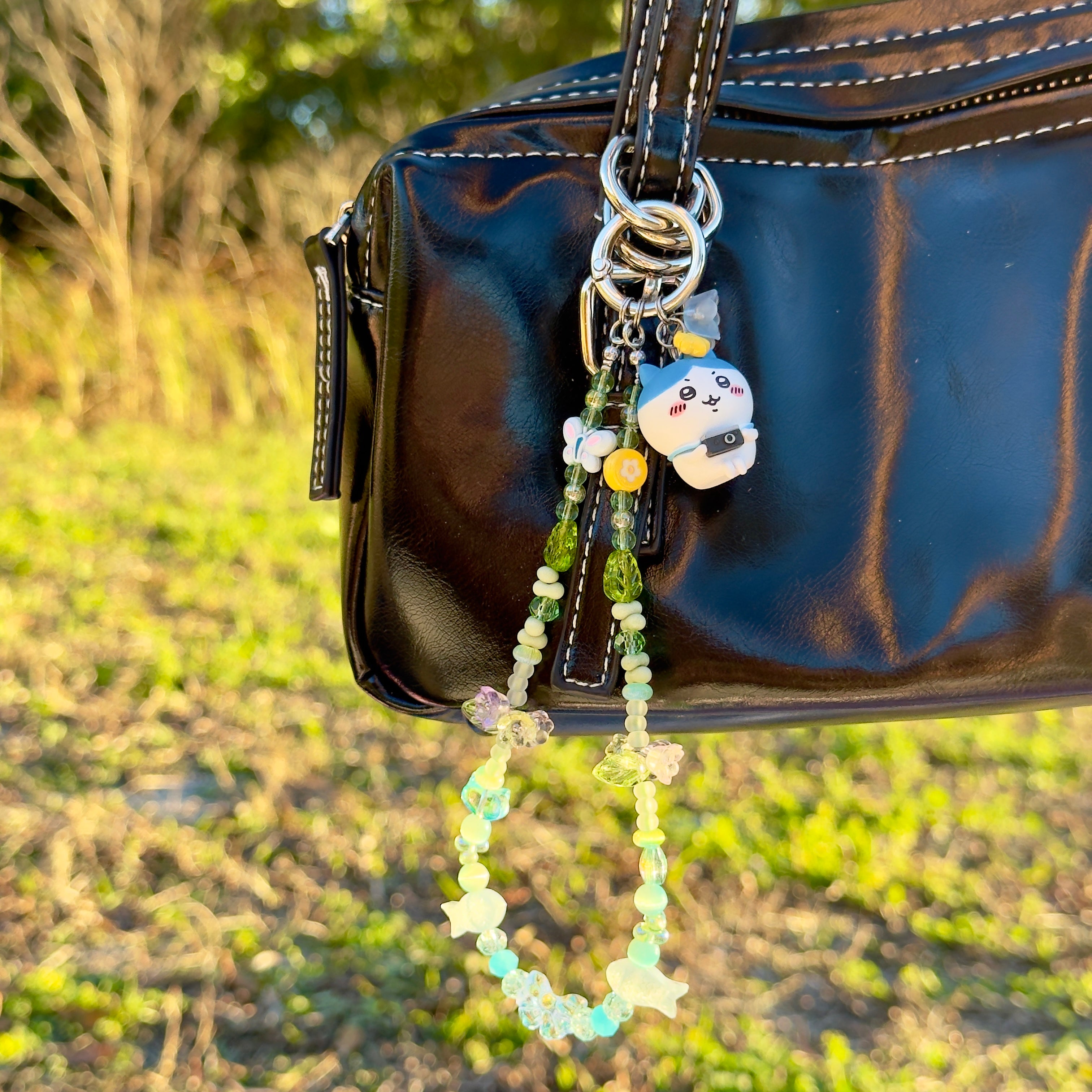 Black handbag with a beaded charm featuring a cartoon character on a grassy background