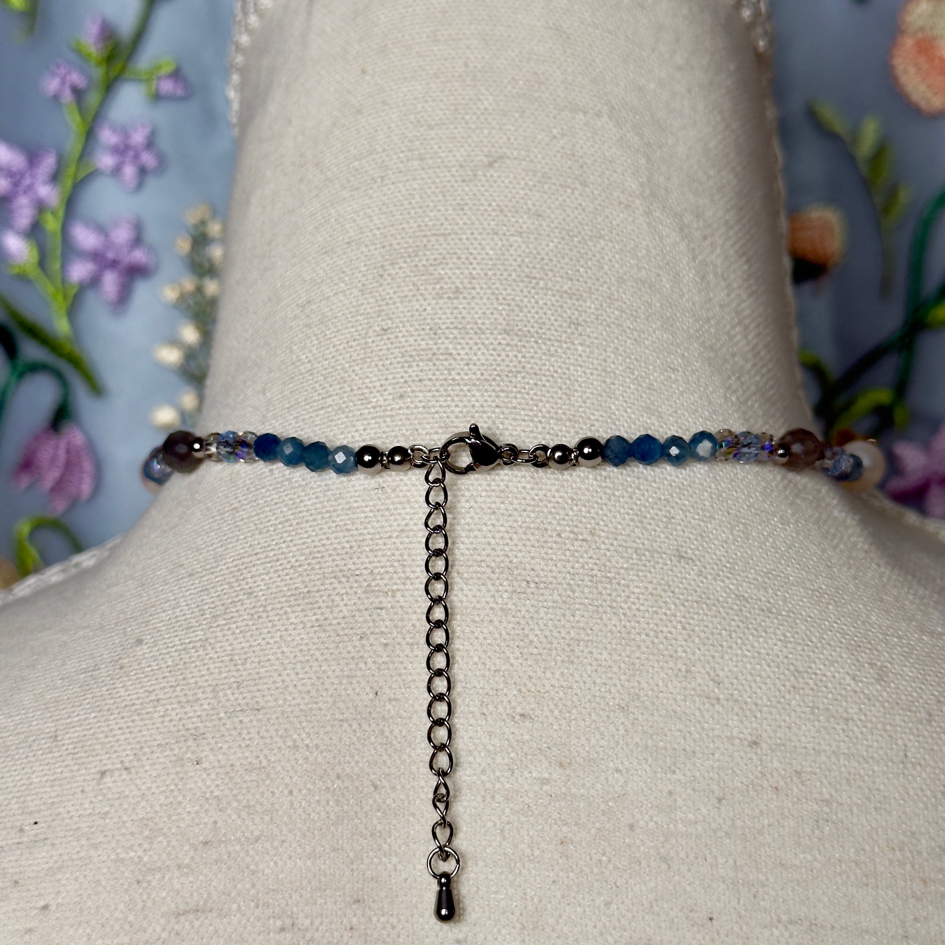 Necklace with blue beads on a mannequin bust against a floral background