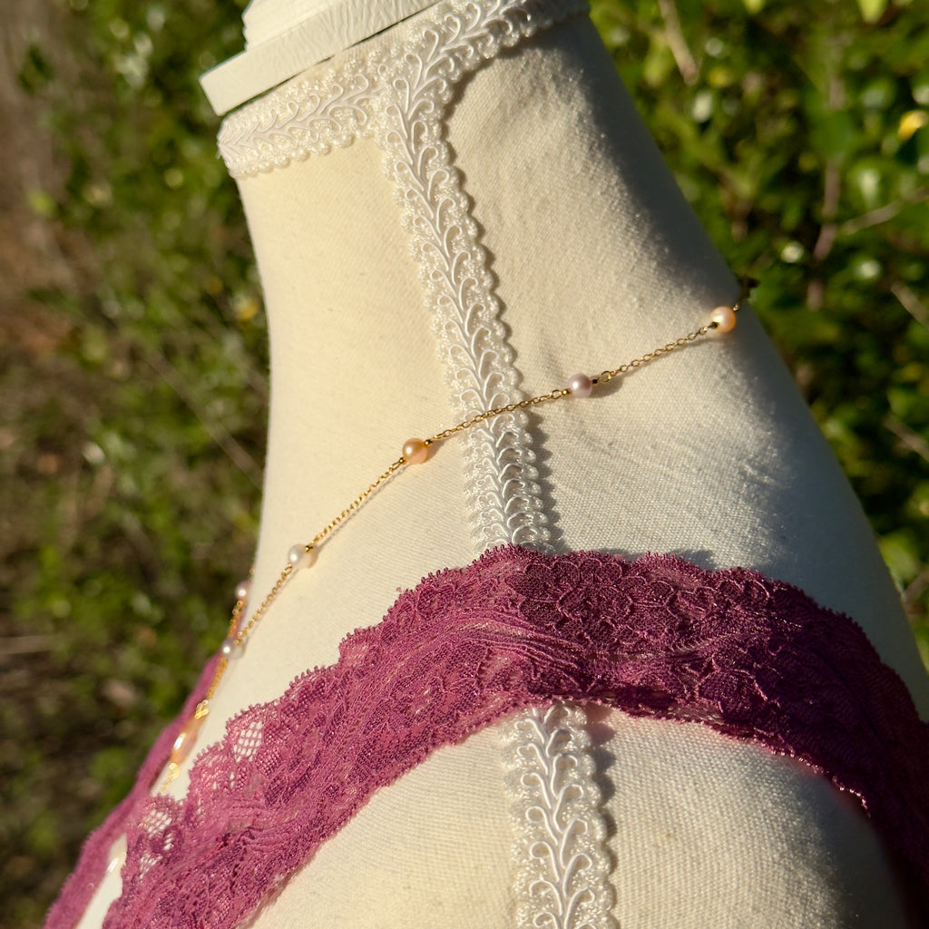 Mannequin wearing a gold chain and purple lace garment with a blurred green background