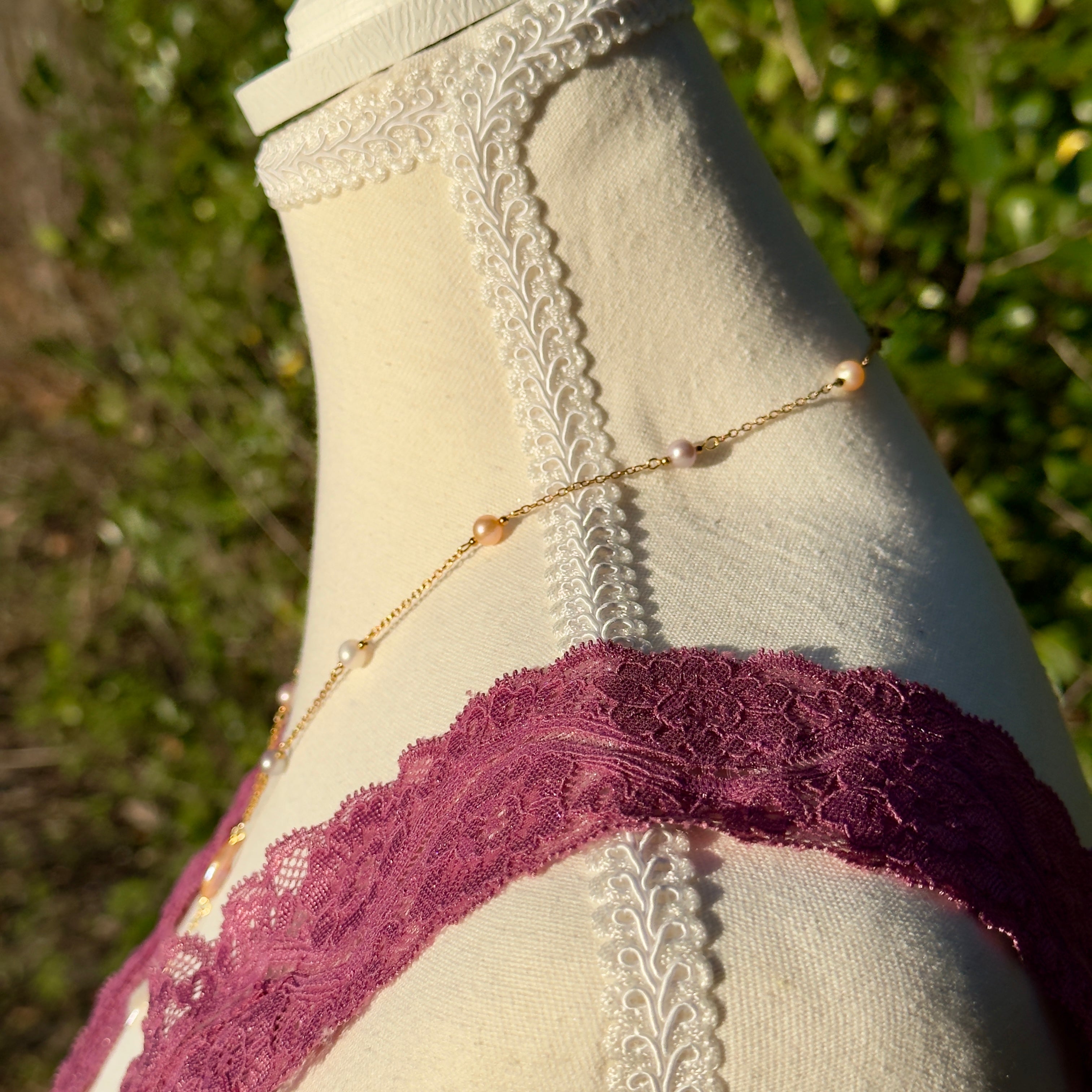 Mannequin wearing a gold chain and purple lace garment with a blurred green background