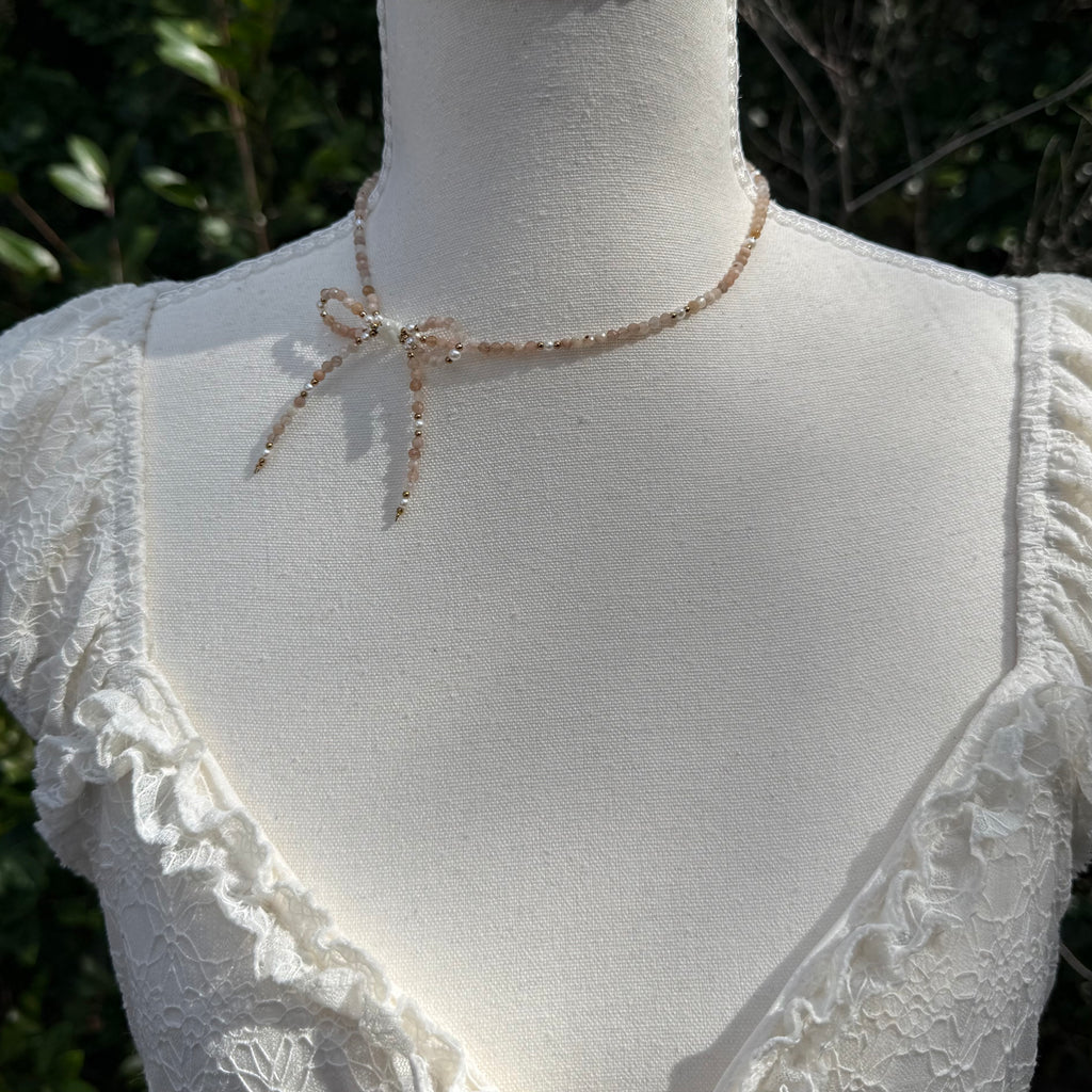 Mannequin wearing a delicate necklace with a white lace top against a natural background