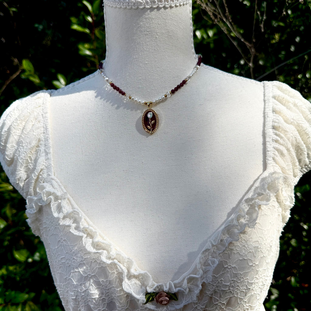 Mannequin wearing a white lace garment with a necklace against a green leafy background